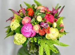 A lush bouquet of pinks, reds and yellows, on display in a deep green ceramic vase