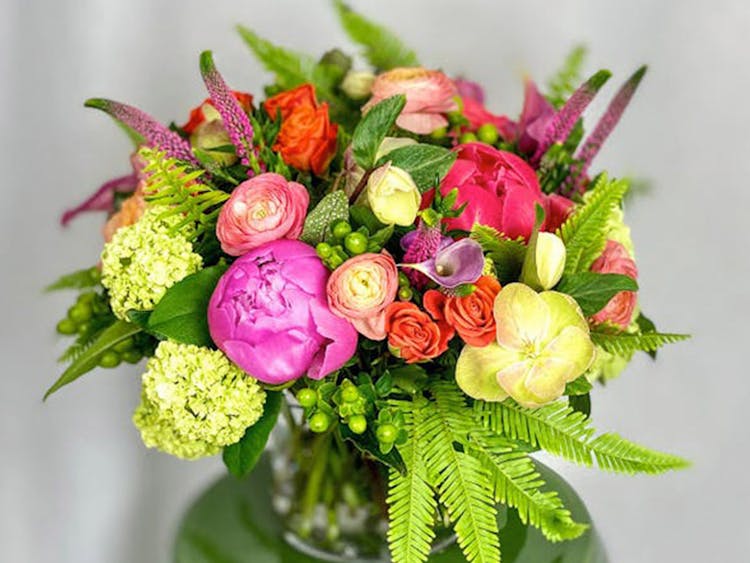 A lush bouquet of pinks, reds and yellows, on display in a deep green ceramic vase